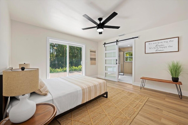 bedroom with light hardwood / wood-style flooring, ceiling fan, and a barn door