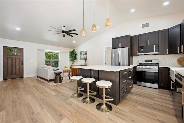 kitchen featuring light wood-type flooring, a center island, ceiling fan, appliances with stainless steel finishes, and a breakfast bar area