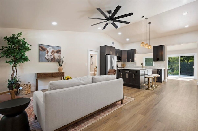 living room featuring sink, ceiling fan, light hardwood / wood-style floors, and vaulted ceiling