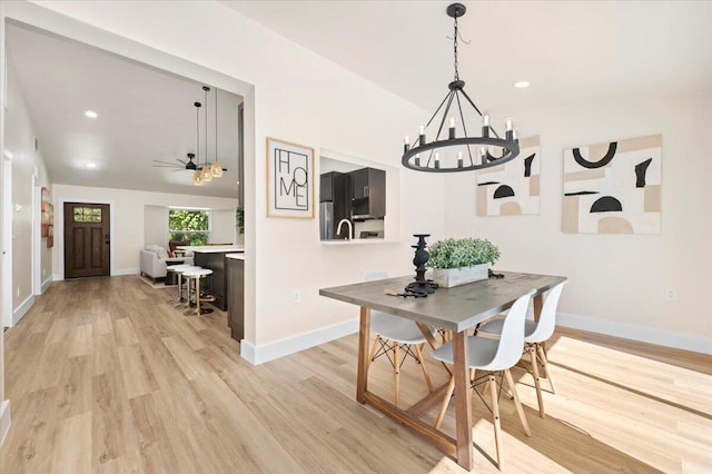 dining room with ceiling fan with notable chandelier, sink, and light hardwood / wood-style flooring