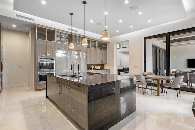 kitchen with a kitchen island with sink, double oven, a sink, modern cabinets, and pendant lighting