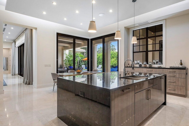 kitchen with dark stone countertops, a center island with sink, hanging light fixtures, a sink, and modern cabinets