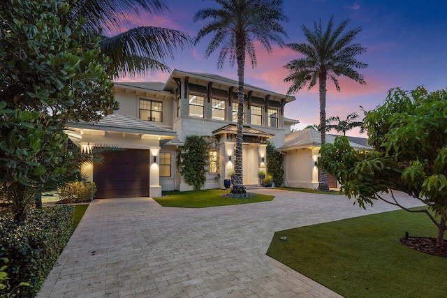 view of front of house featuring stucco siding, a yard, decorative driveway, and a garage