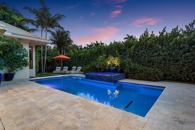 pool at dusk featuring a pool with connected hot tub and a patio area