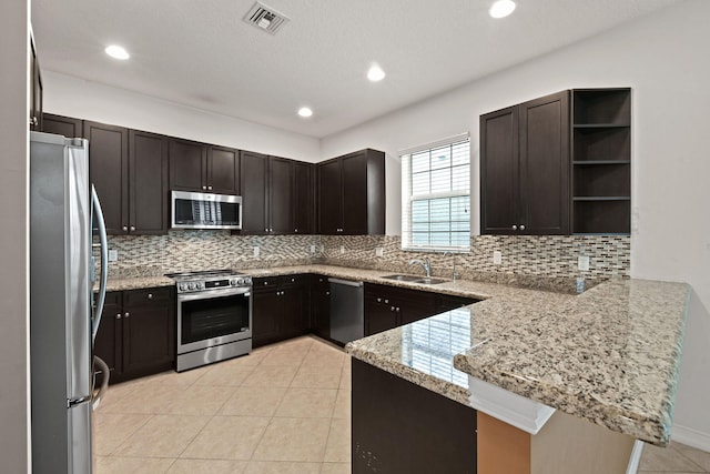 kitchen with decorative backsplash, kitchen peninsula, stainless steel appliances, sink, and light stone counters