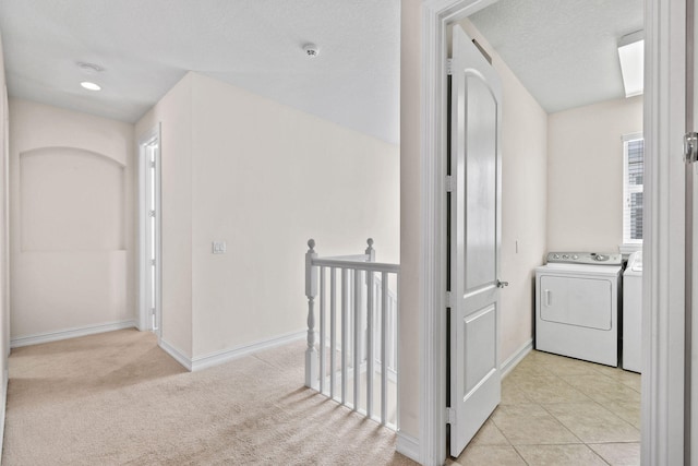 hall featuring a textured ceiling, washing machine and clothes dryer, and light colored carpet