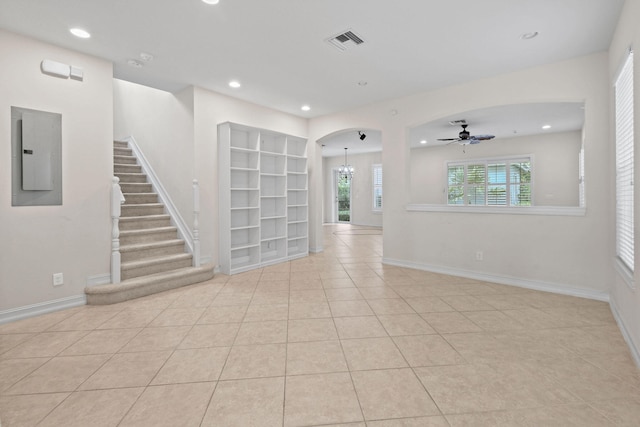 tiled spare room with built in features, electric panel, and ceiling fan with notable chandelier