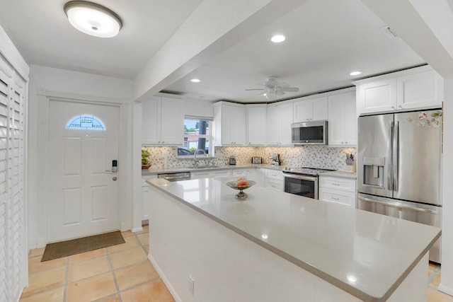 kitchen featuring appliances with stainless steel finishes, white cabinets, light tile patterned floors, a center island, and ceiling fan