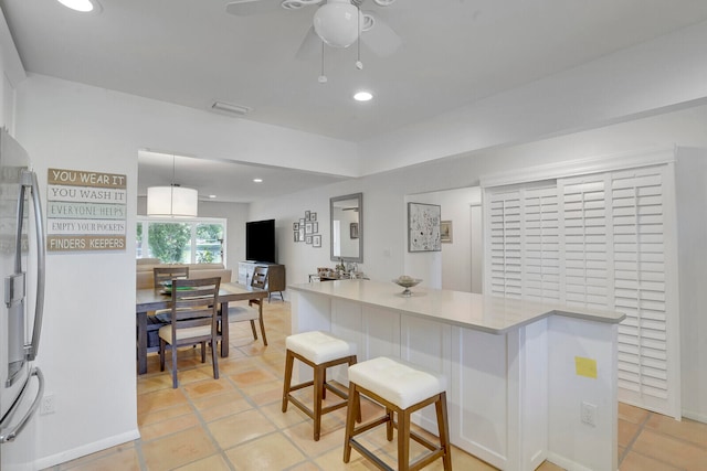 kitchen with stainless steel fridge, ceiling fan, light tile patterned floors, and a kitchen bar