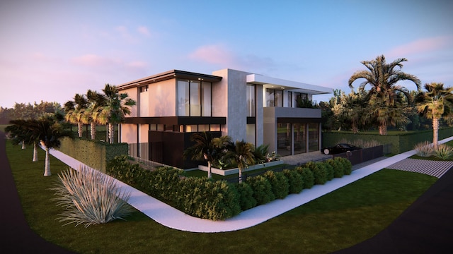 back house at dusk featuring a balcony and a yard