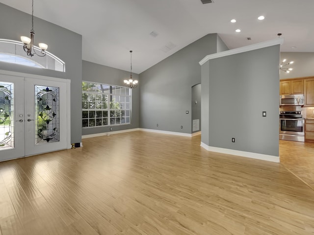 unfurnished living room with high vaulted ceiling, light wood-type flooring, and an inviting chandelier