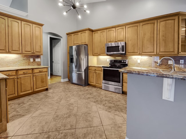 kitchen with stainless steel appliances, a notable chandelier, backsplash, high vaulted ceiling, and light tile patterned flooring