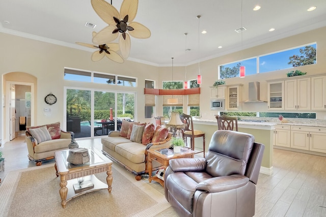 living room featuring a towering ceiling, ceiling fan, ornamental molding, and light wood-type flooring