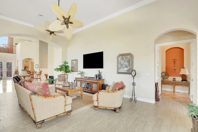 living room with ceiling fan, a towering ceiling, crown molding, and light tile patterned floors