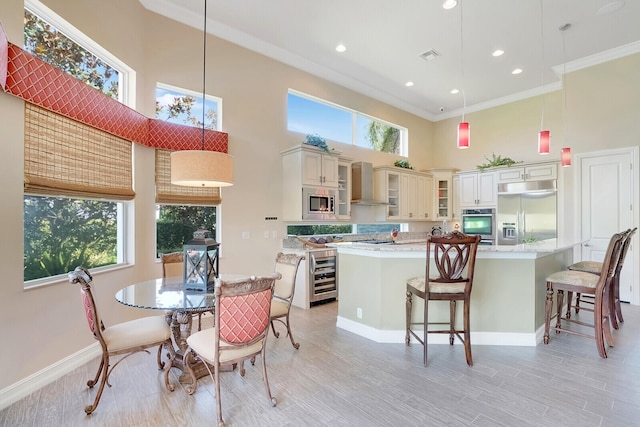 kitchen with wall chimney range hood, built in appliances, a high ceiling, ornamental molding, and decorative light fixtures