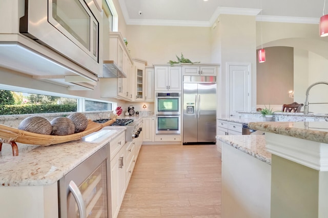 kitchen featuring light stone counters, light hardwood / wood-style floors, crown molding, built in appliances, and hanging light fixtures