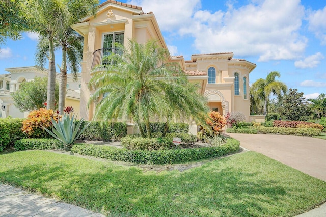 mediterranean / spanish-style home featuring a tile roof, driveway, a front lawn, and stucco siding