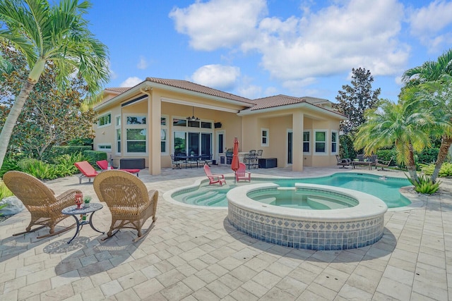 back of property with a tile roof, a patio, stucco siding, a pool with connected hot tub, and a ceiling fan