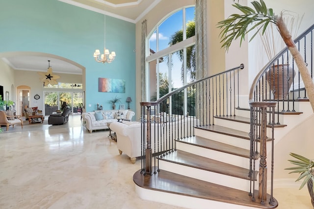 stairs featuring ceiling fan with notable chandelier, ornamental molding, a towering ceiling, and tile patterned floors