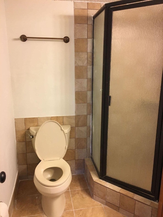 bathroom with a shower with shower door, tile walls, toilet, and tile patterned flooring