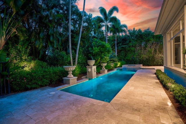 pool at dusk with an in ground hot tub and a patio area