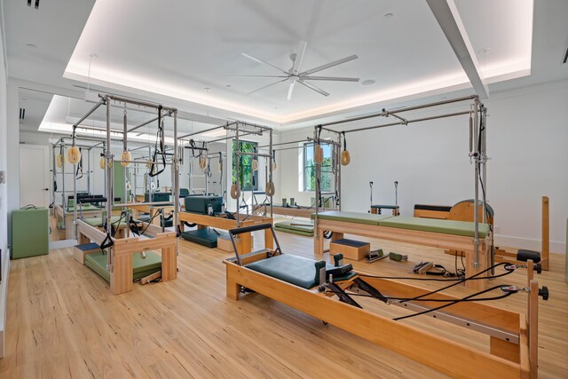 workout area with ceiling fan, a raised ceiling, and light wood-type flooring