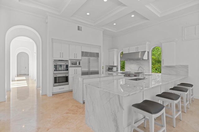 kitchen with decorative backsplash, built in appliances, coffered ceiling, light stone countertops, and beamed ceiling