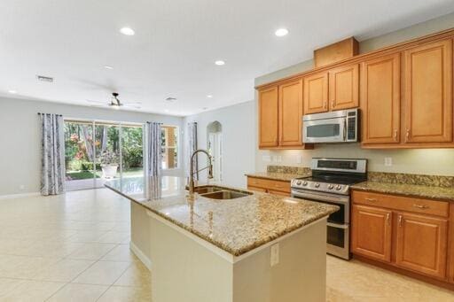 kitchen featuring ceiling fan, light stone countertops, sink, stainless steel appliances, and a center island with sink