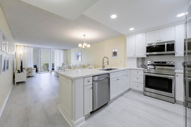 kitchen featuring kitchen peninsula, appliances with stainless steel finishes, sink, a textured ceiling, and an inviting chandelier