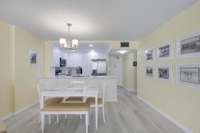 dining room featuring light wood-type flooring, sink, a textured ceiling, and a chandelier