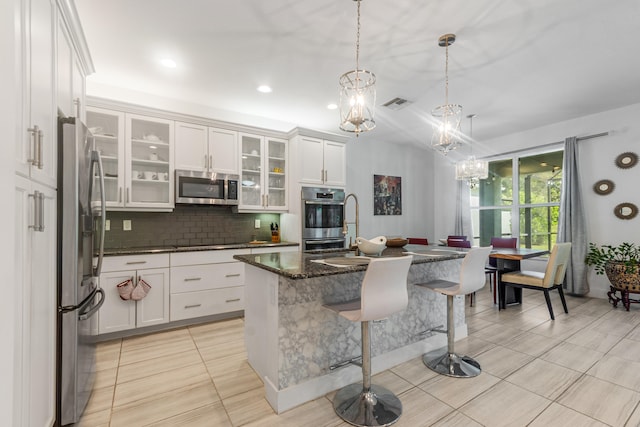 kitchen featuring a kitchen breakfast bar, tasteful backsplash, decorative light fixtures, a center island with sink, and stainless steel appliances