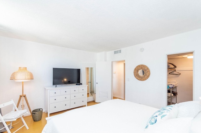 bedroom with a textured ceiling, light hardwood / wood-style flooring, a spacious closet, and a closet