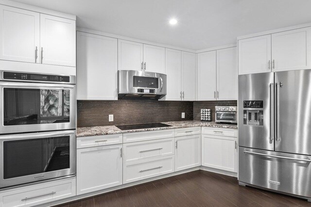 kitchen with dark hardwood / wood-style flooring, tasteful backsplash, white cabinetry, light stone countertops, and stainless steel appliances