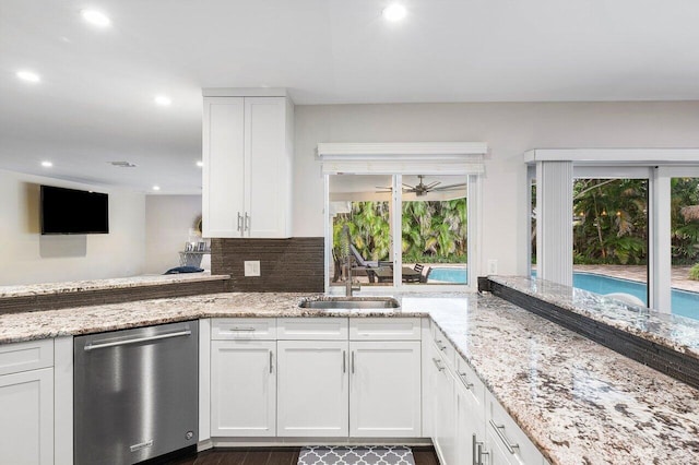 kitchen with dishwasher, backsplash, light stone countertops, white cabinetry, and a sink