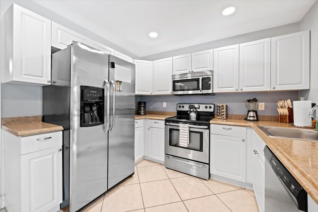 kitchen with stainless steel appliances, sink, white cabinets, and light tile patterned flooring