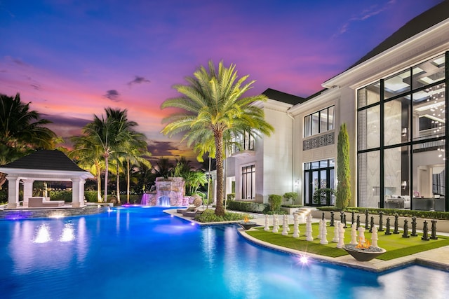 pool at dusk with french doors, a gazebo, and pool water feature