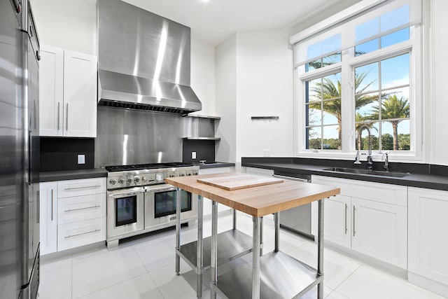 kitchen with wall chimney range hood, decorative backsplash, white cabinets, double oven range, and sink