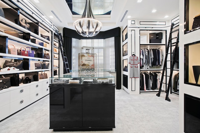 walk in closet featuring a raised ceiling, an inviting chandelier, and light colored carpet