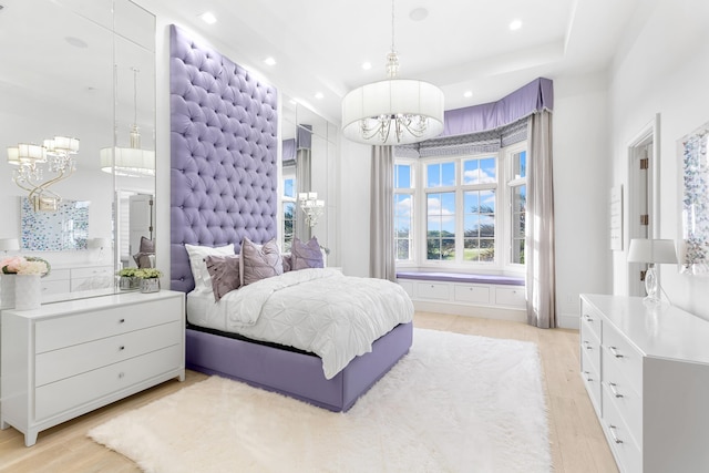 bedroom with a raised ceiling, an inviting chandelier, and light hardwood / wood-style flooring