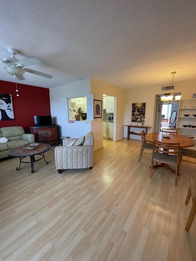 living room with light hardwood / wood-style floors, ceiling fan with notable chandelier, and a textured ceiling