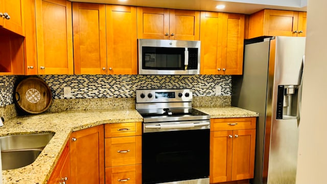 kitchen with light stone countertops, appliances with stainless steel finishes, tasteful backsplash, and sink