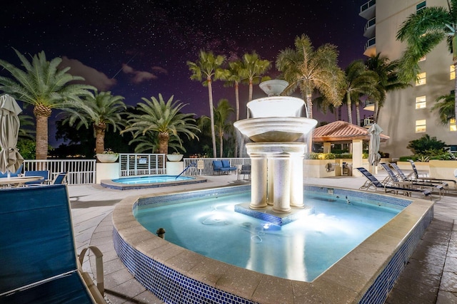 pool at night with a patio area, a gazebo, and a hot tub