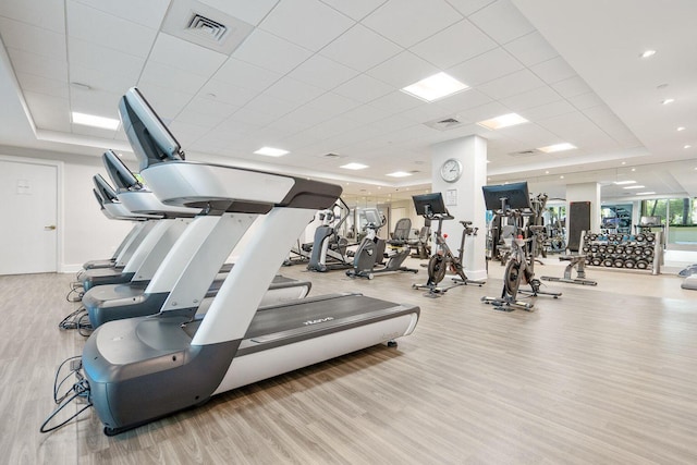 exercise room featuring a tray ceiling, light hardwood / wood-style floors, and a drop ceiling