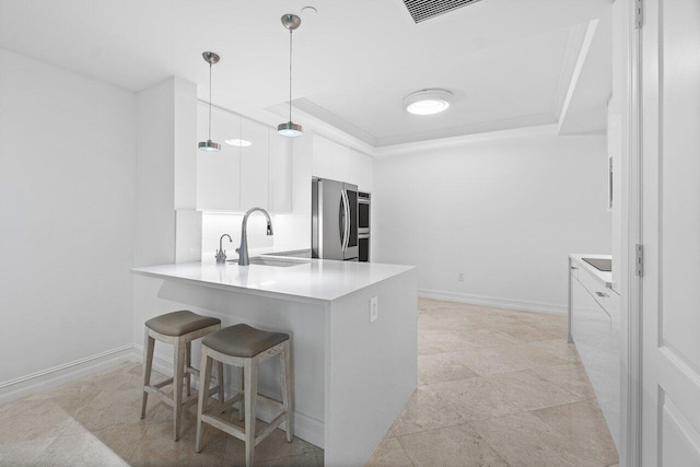 kitchen featuring pendant lighting, a kitchen bar, stainless steel refrigerator, sink, and white cabinets