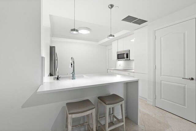 kitchen with decorative light fixtures, a breakfast bar, kitchen peninsula, stainless steel appliances, and white cabinets