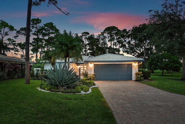 view of front of property with a garage, a tile roof, decorative driveway, a front yard, and stucco siding