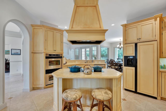 kitchen featuring arched walkways, light tile patterned floors, light countertops, paneled built in fridge, and a kitchen bar