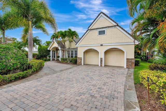 view of front of property with a garage, decorative driveway, stone siding, and stucco siding