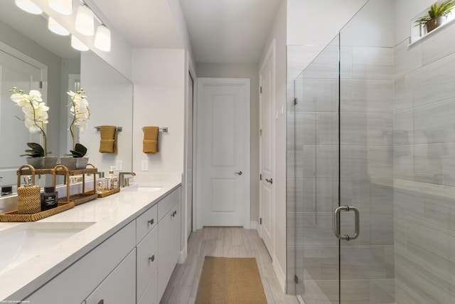 full bath with double vanity, wood finish floors, a sink, and a shower stall