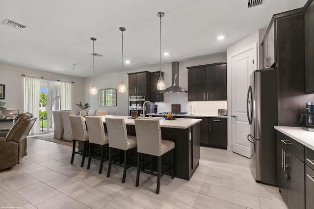 kitchen with visible vents, stainless steel appliances, light countertops, wall chimney range hood, and a kitchen bar